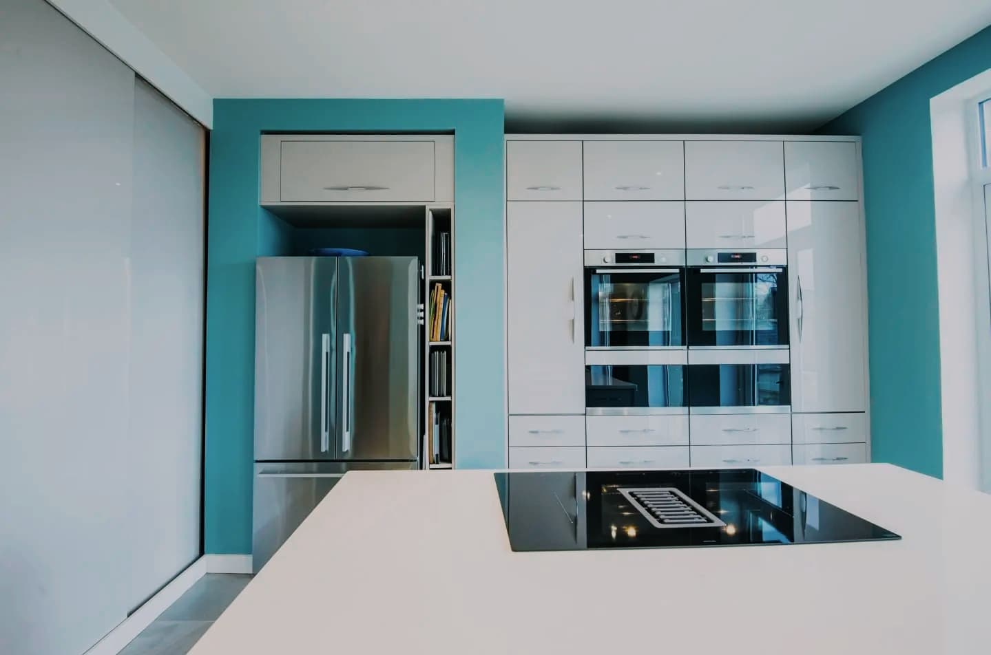 Modern kitchen with teal feature wall, integrated fridge freezer and built-in ovens