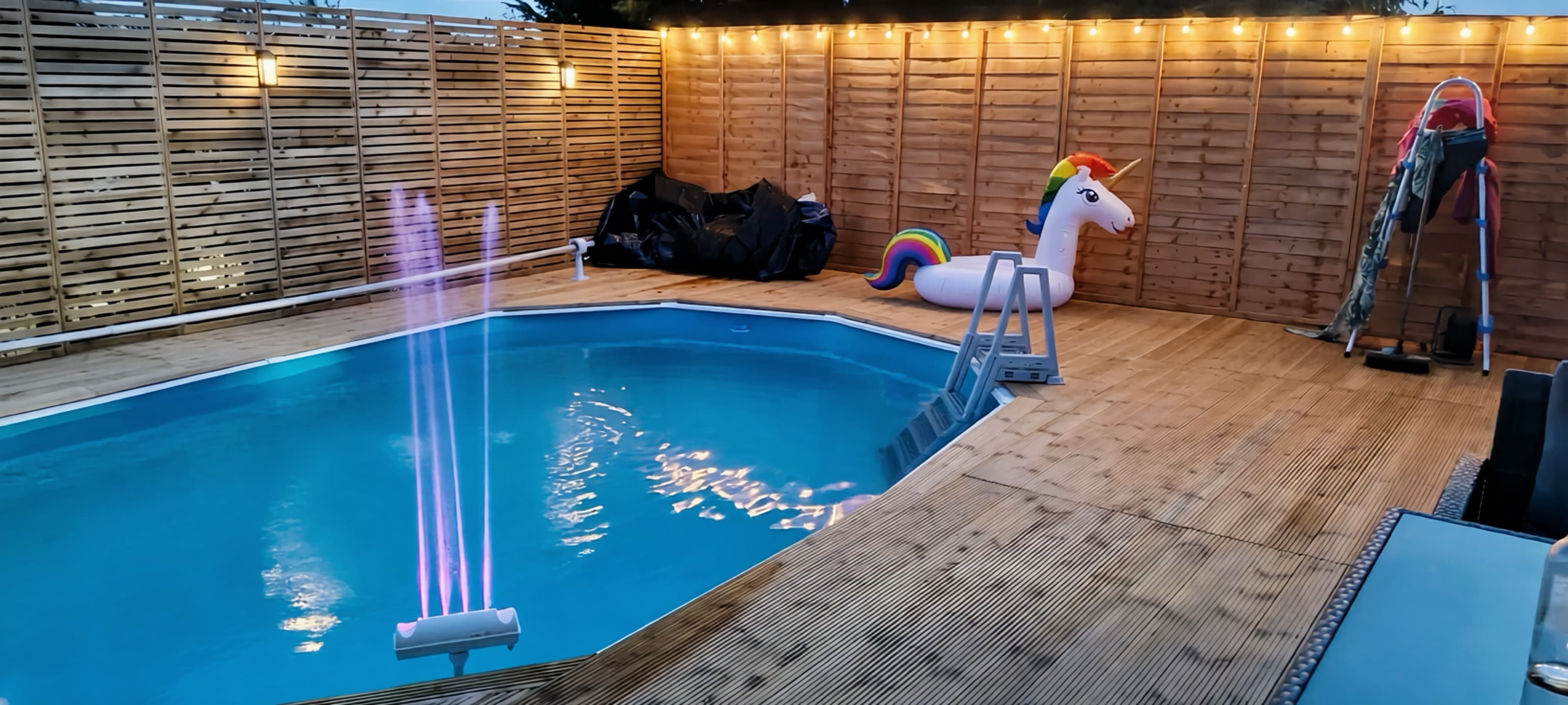 Outdoor swimming pool with timber decking and festoon lighting at dusk